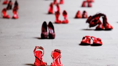 Auf einem Platz stehen in unregelmäßigen Abständen unterschiedliche rote Frauenschuhe.