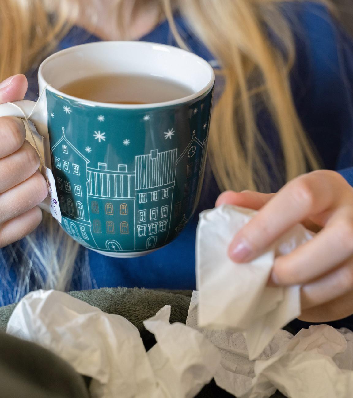 Symbolbild:  Eine Frau trinkt Tee und hält ein Taschentuch in ihrer Hand. 