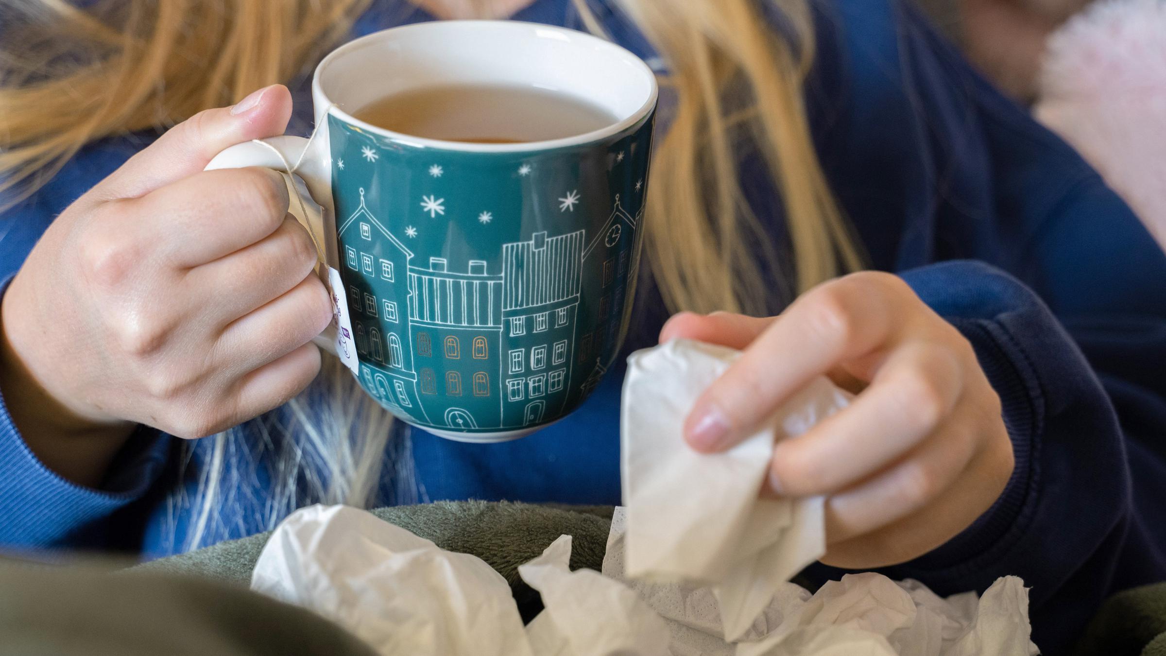 Symbolbild:  Eine Frau trinkt Tee und hält ein Taschentuch in ihrer Hand. 