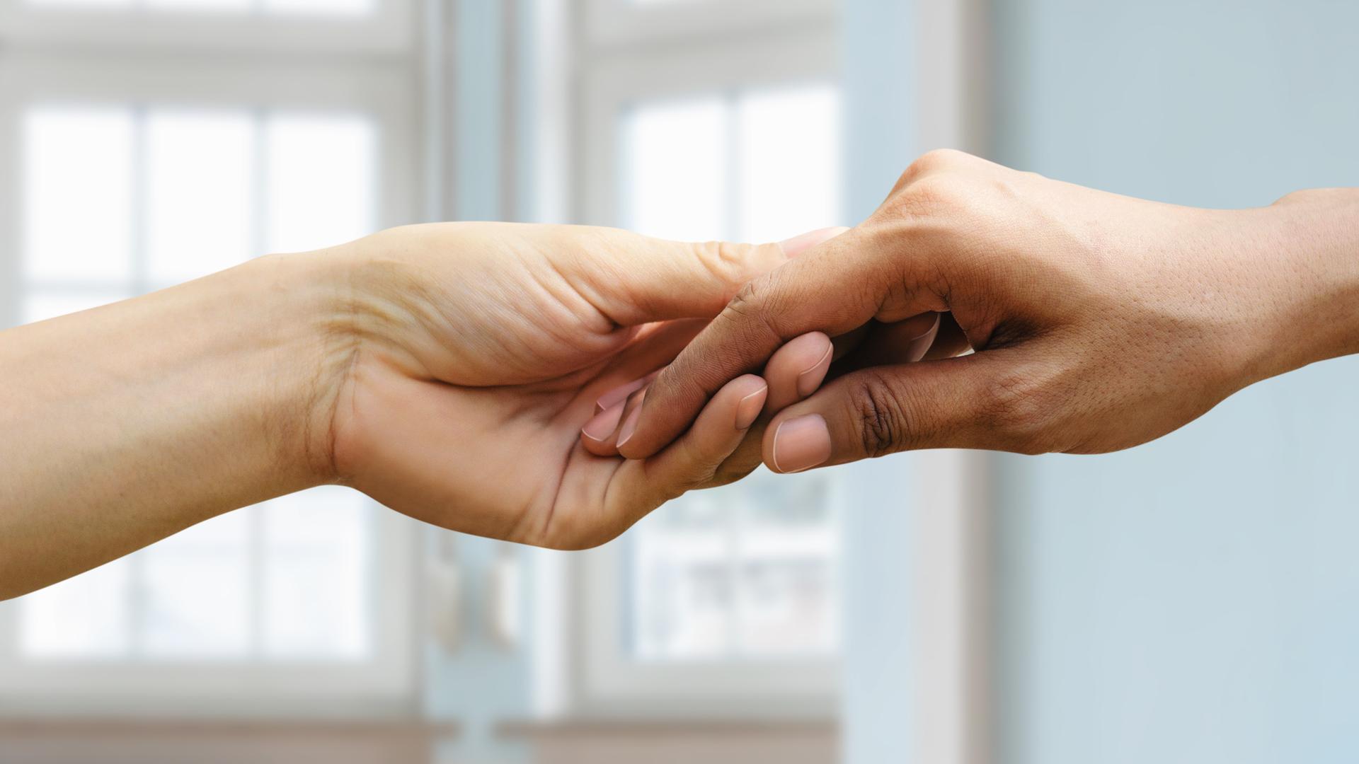 Zwei Hände unterschiedlicher Hautfarbe halten einander