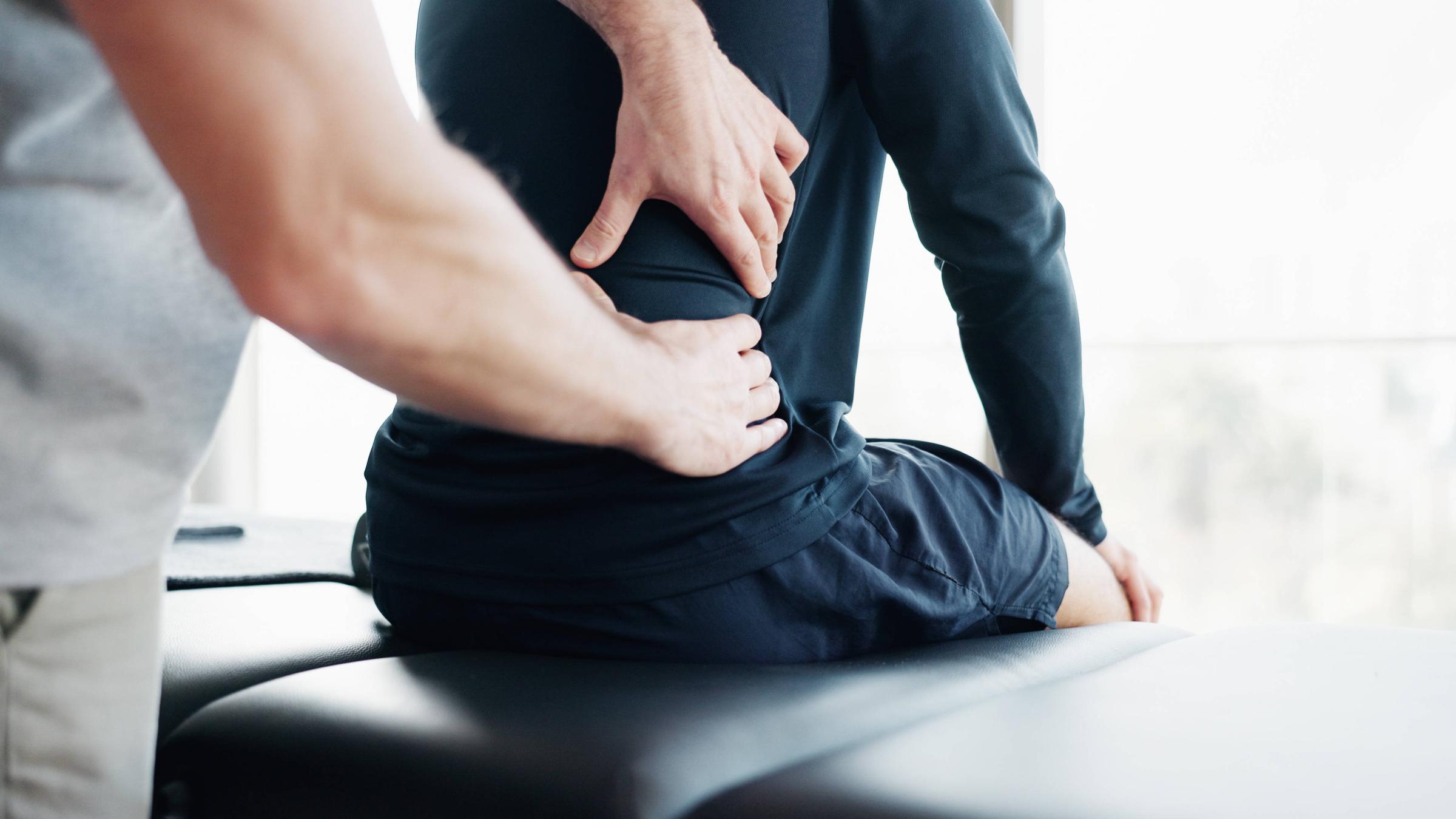 Eine Person sitzt auf einer Arztliege und wird am Rücken untersucht.