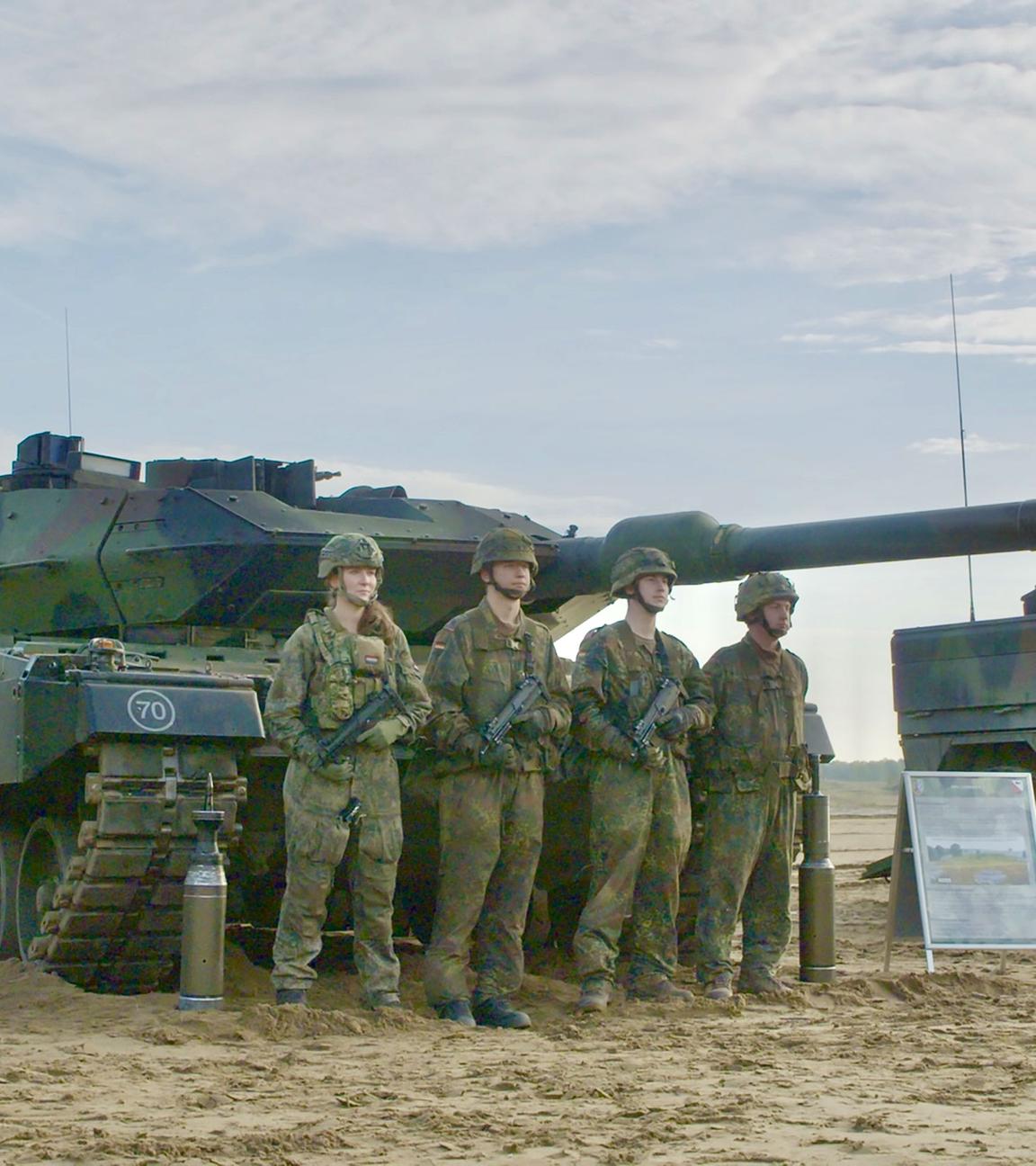 Vier Soldaten der Bundeswehr stehen in Tarnuniform vor einem Leopard 2 Panzer. Daneben steht ein weiterer Panzer.