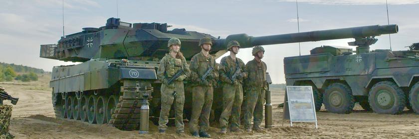 Vier Soldaten der Bundeswehr stehen in Tarnuniform vor einem Leopard 2 Panzer. Daneben steht ein weiterer Panzer.