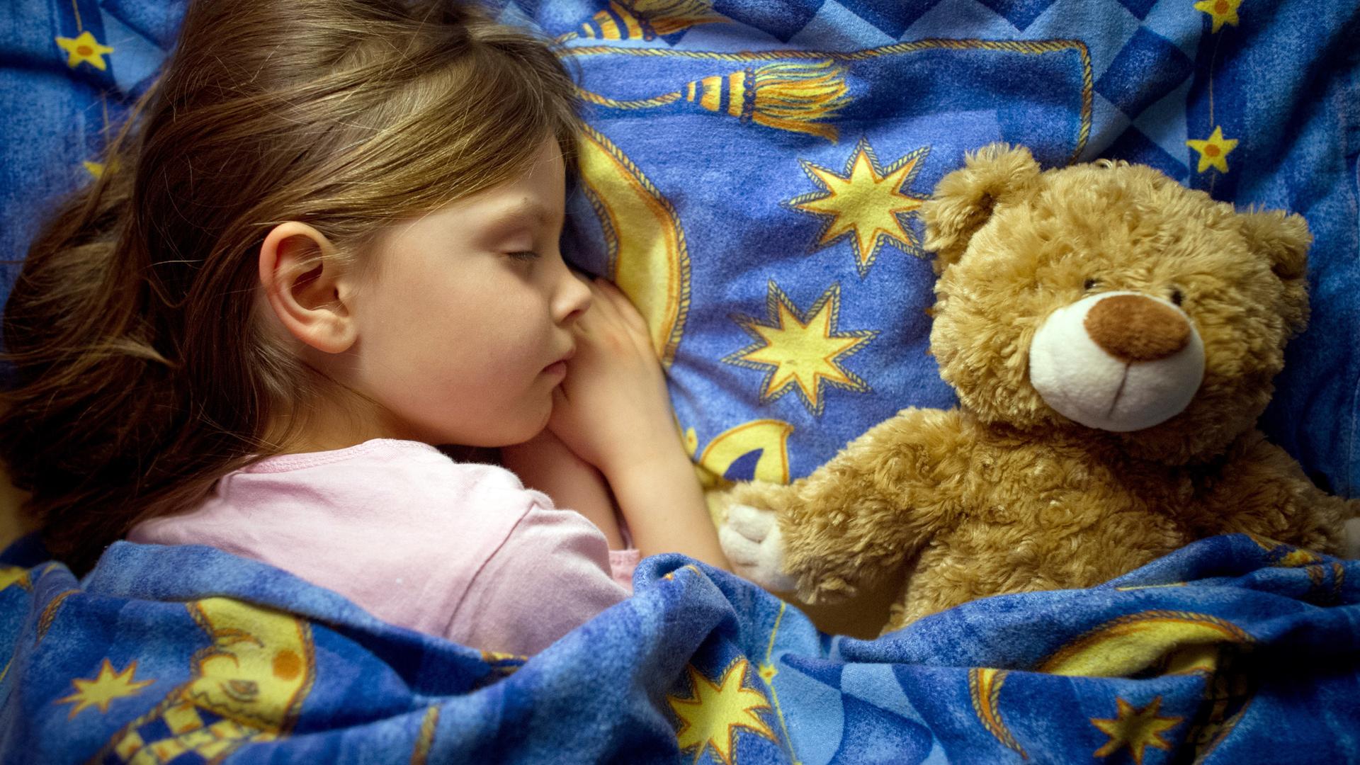 Schlafendes Kind neben einem Teddybären.