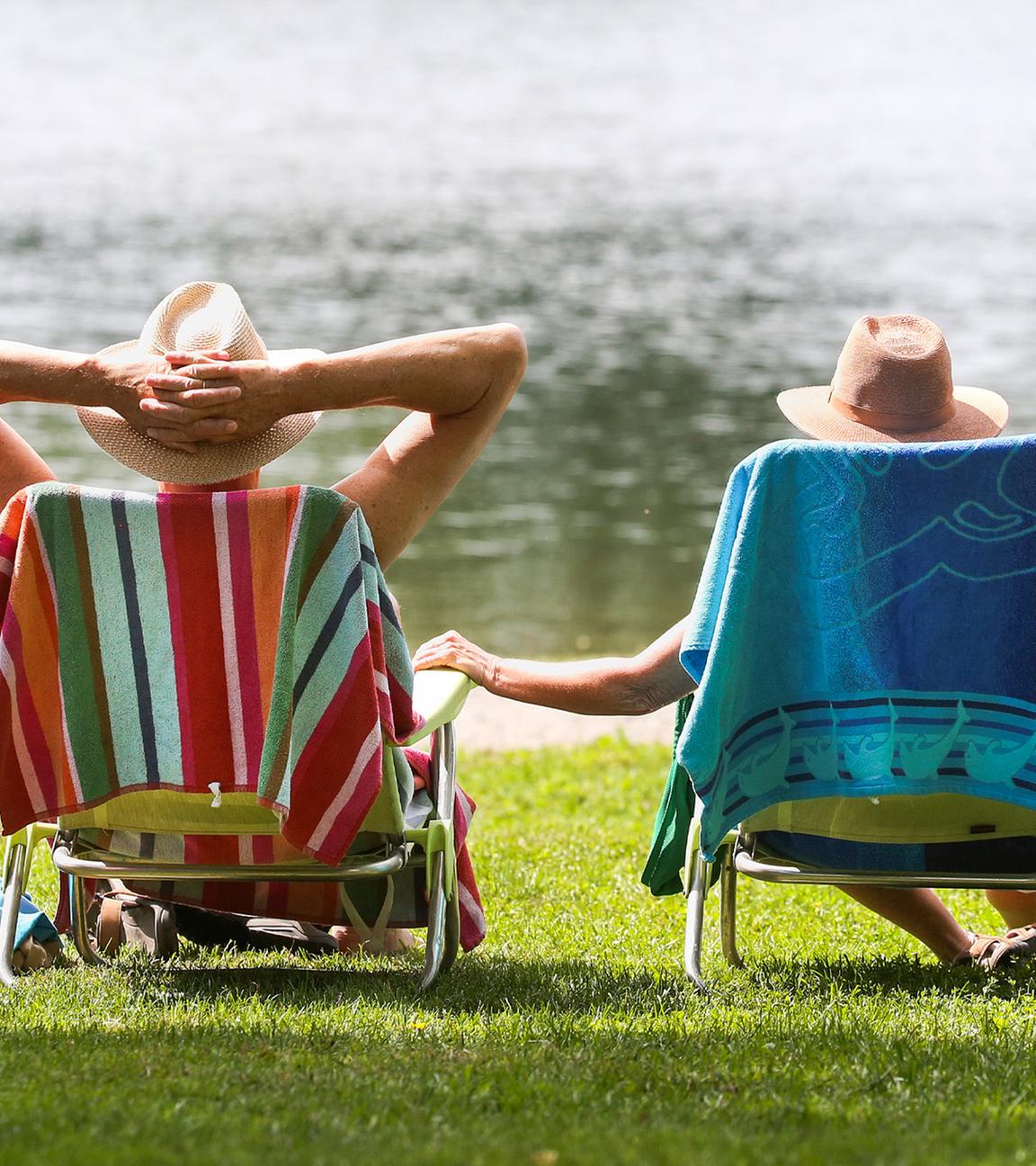 Ein Mann und eine Frau mit Strohhüten sitzen an einem Badesee in ihren Stühlen in der Sonne. (Archiv)