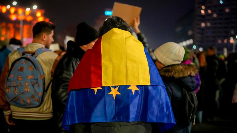 Ein Mann mit der rumänischen und der EU-Fahne über den Schultern nimmt an einem Protest gegen Georgescu, den unabhängigen Kandidaten für das rumänische Präsidentenamt, der die erste Wahlrunde gewonnen hat.