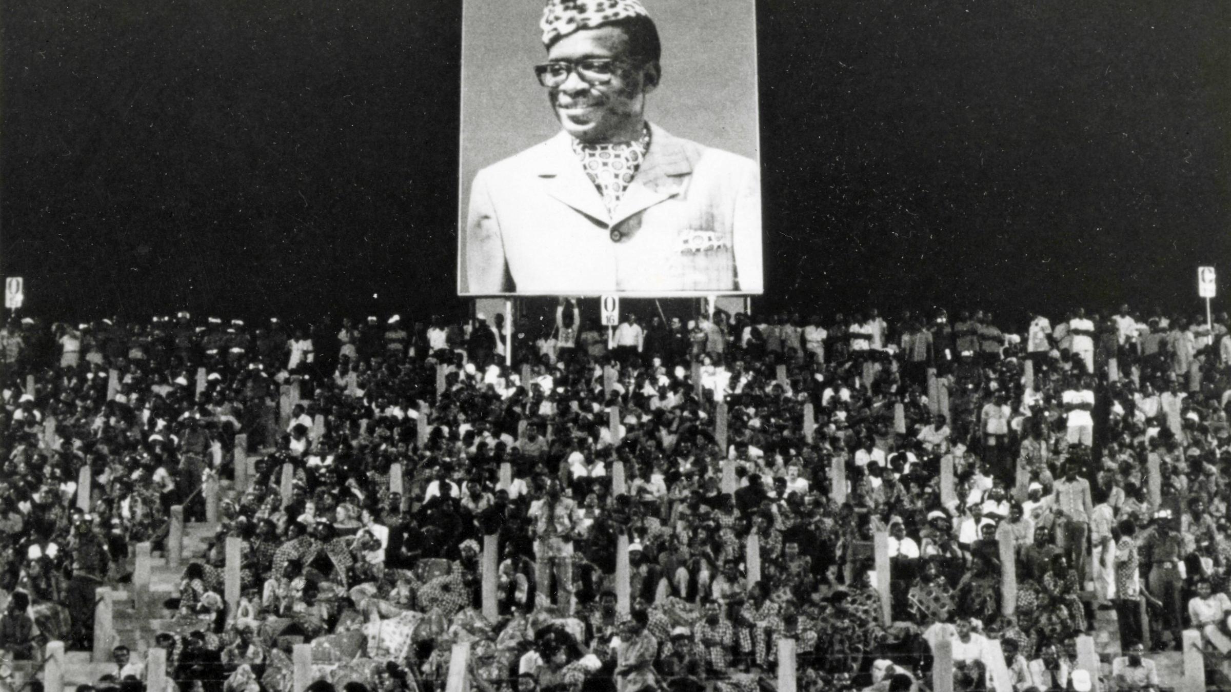 Zuschauer unter einem Plakat von Zaires Präsident Mobutu beim Boxkampft George Foreman - Muhammad Ali am 30. Oktober 1974 in Kinshasa