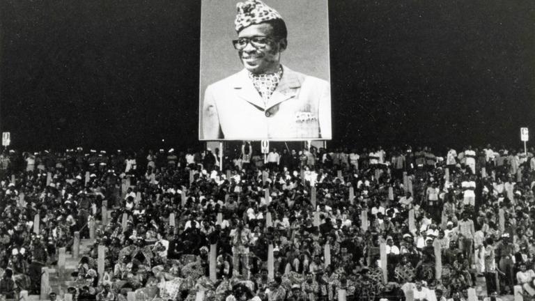 Zuschauer unter einem Plakat von Zaires Präsident Mobutu beim Boxkampft George Foreman - Muhammad Ali am 30. Oktober 1974 in Kinshasa