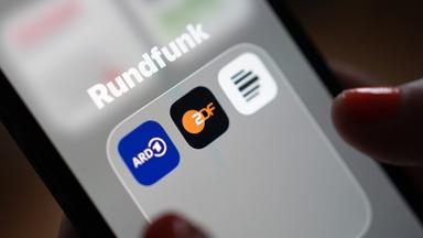 Auf dem Bildschirm eines Smartphones sind die App-Icons von ARD, ZDF und Deutschlandfunk im Ordner "Rundfunk" zu sehen.