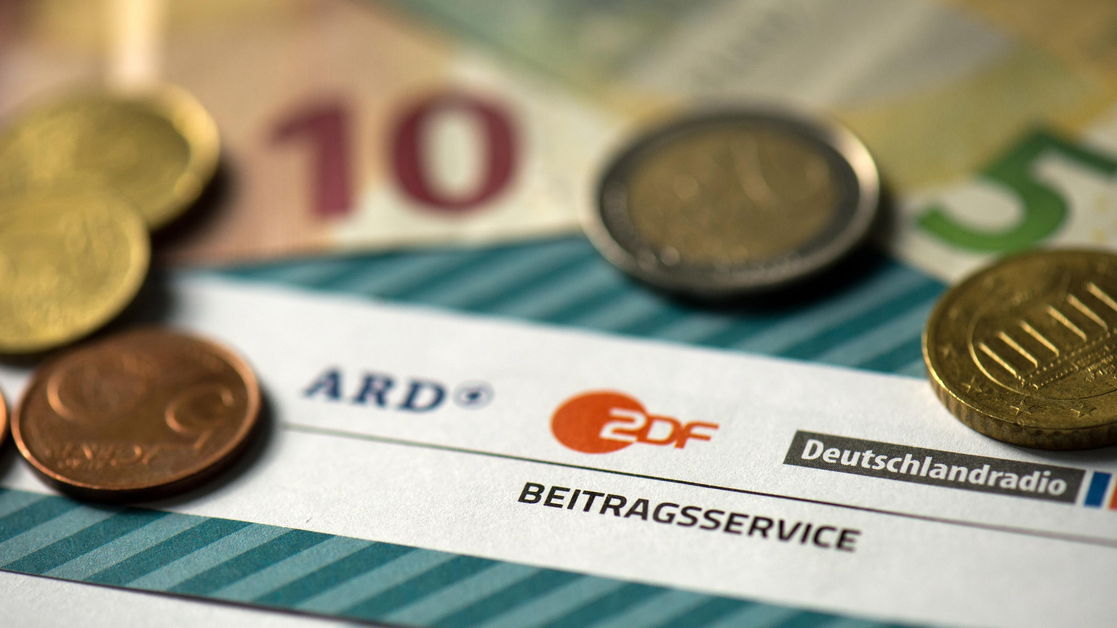 Archiv: Symbolbild zum Rundfunkbeitrag. Geldmünzen und Scheine liegen neben einem ARD/ ZDF Dokument. Am 15.04.16 in Dresden.