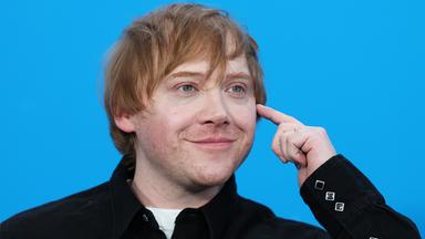 Rupert Grint ist lächelnd vor blauem Hintergrund zu sehen.