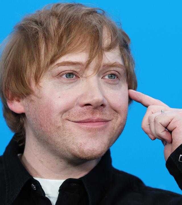 Rupert Grint ist lächelnd vor blauem Hintergrund zu sehen.