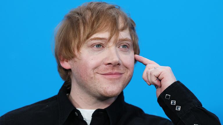 Rupert Grint ist lächelnd vor blauem Hintergrund zu sehen.