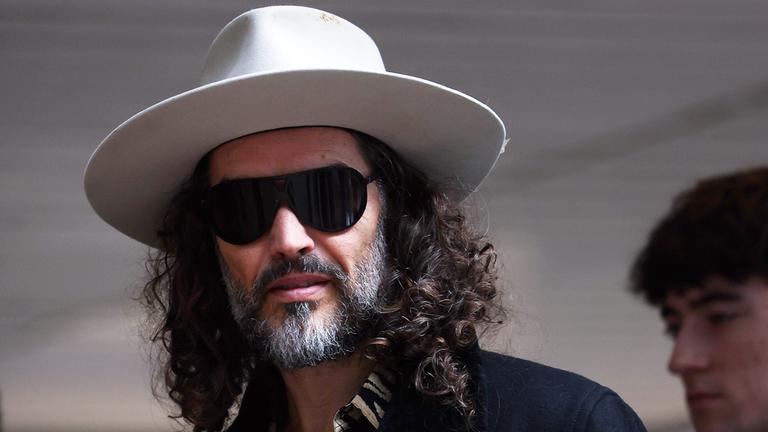 Russel Brand posiert mit Sonnenbrille und einem großen Hut.