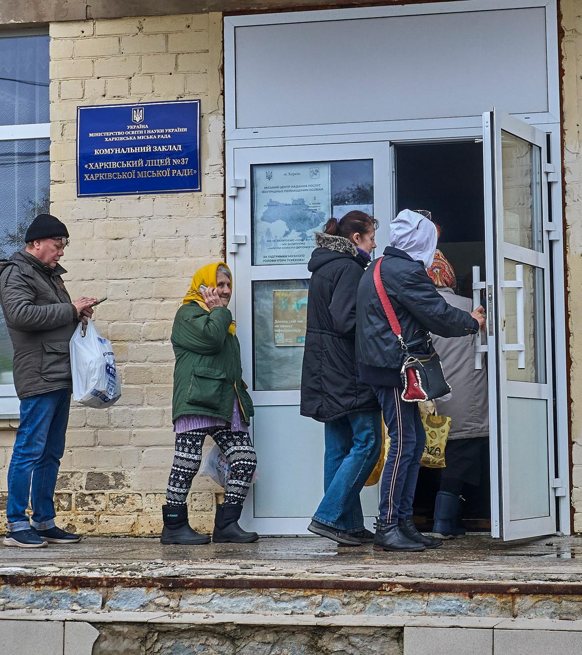  Ukrainians line up to receive a hot meal during a food aid distribution in a school in Kharkiv
