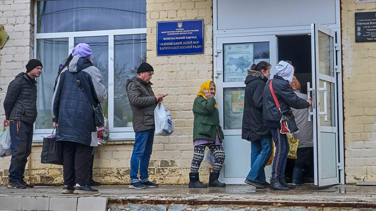  Ukrainians line up to receive a hot meal during a food aid distribution in a school in Kharkiv