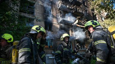Ukrainische Feuerwehrleute mit Sauerstoffflaschen und Helmen bereiten sich in Kiew darauf vor, ein brennendes Wohnhaus zu betreten.
