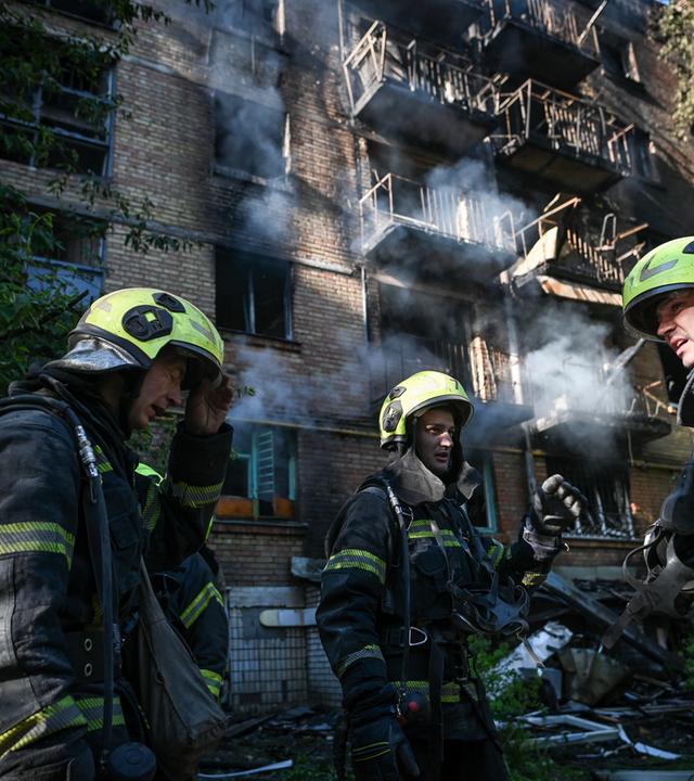 Ukrainische Feuerwehrleute mit Sauerstoffflaschen und Helmen bereiten sich in Kiew darauf vor, ein brennendes Wohnhaus zu betreten.
