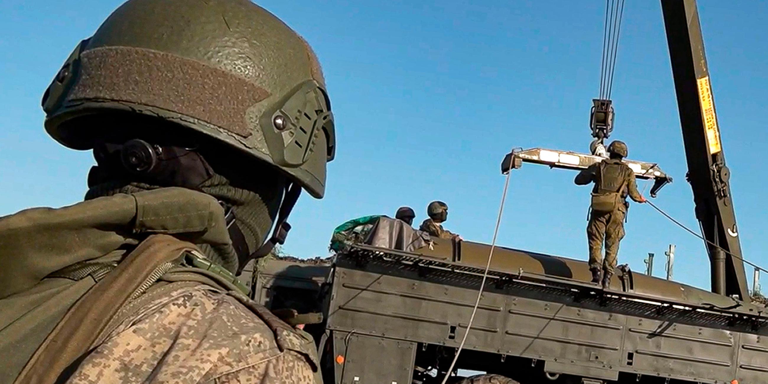 Ein russischer Soldat im Vordergrund bei einer Militärübung, im Hintergrund ein Militärfahrzeug mit Kran.