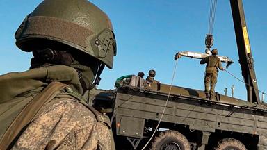 Ein russischer Soldat im Vordergrund bei einer Militärübung, im Hintergrund ein Militärfahrzeug mit Kran.