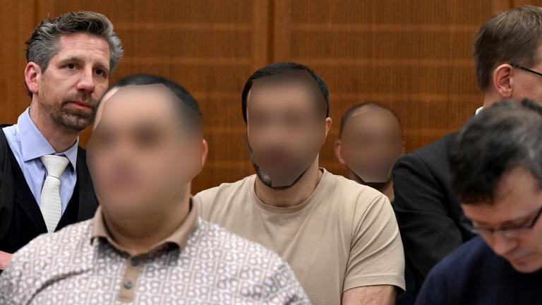 09.12.2025, Hessen, Frankfurt/Main: Die drei Angeklagten, der Ukrainer Robert A. (2.v.l), der Armenier Vardges I (3.v.l) und der Russe Arman S. (4.v.l), warten neben ihren Anwälten im Gerichtssaal auf den Beginn des Prozesses. 