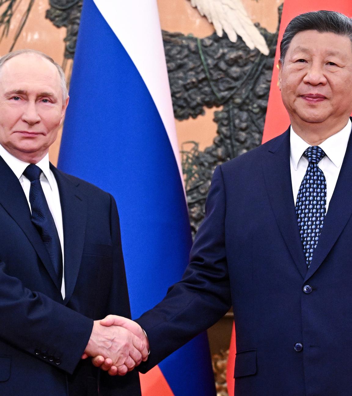 Der russische Präsident Putin und der chinesische Präsident Xi, wie sie sich die Hände schütteln vor den Flaggen von Russland und China