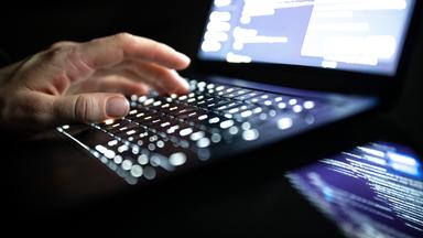 Eine Person tippt mit den Fingern auf einer beleuchteten Laptop-Tastatur. (gestellte Szene)