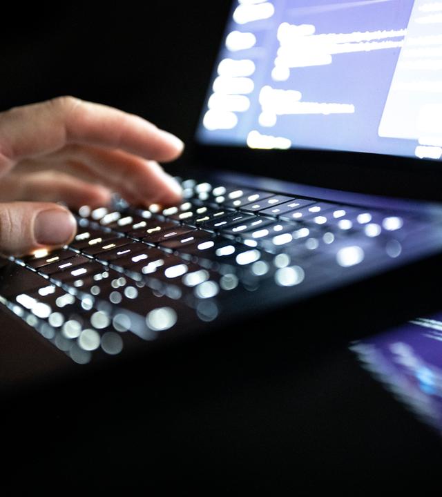 Eine Person tippt mit den Fingern auf einer beleuchteten Laptop-Tastatur. (gestellte Szene)