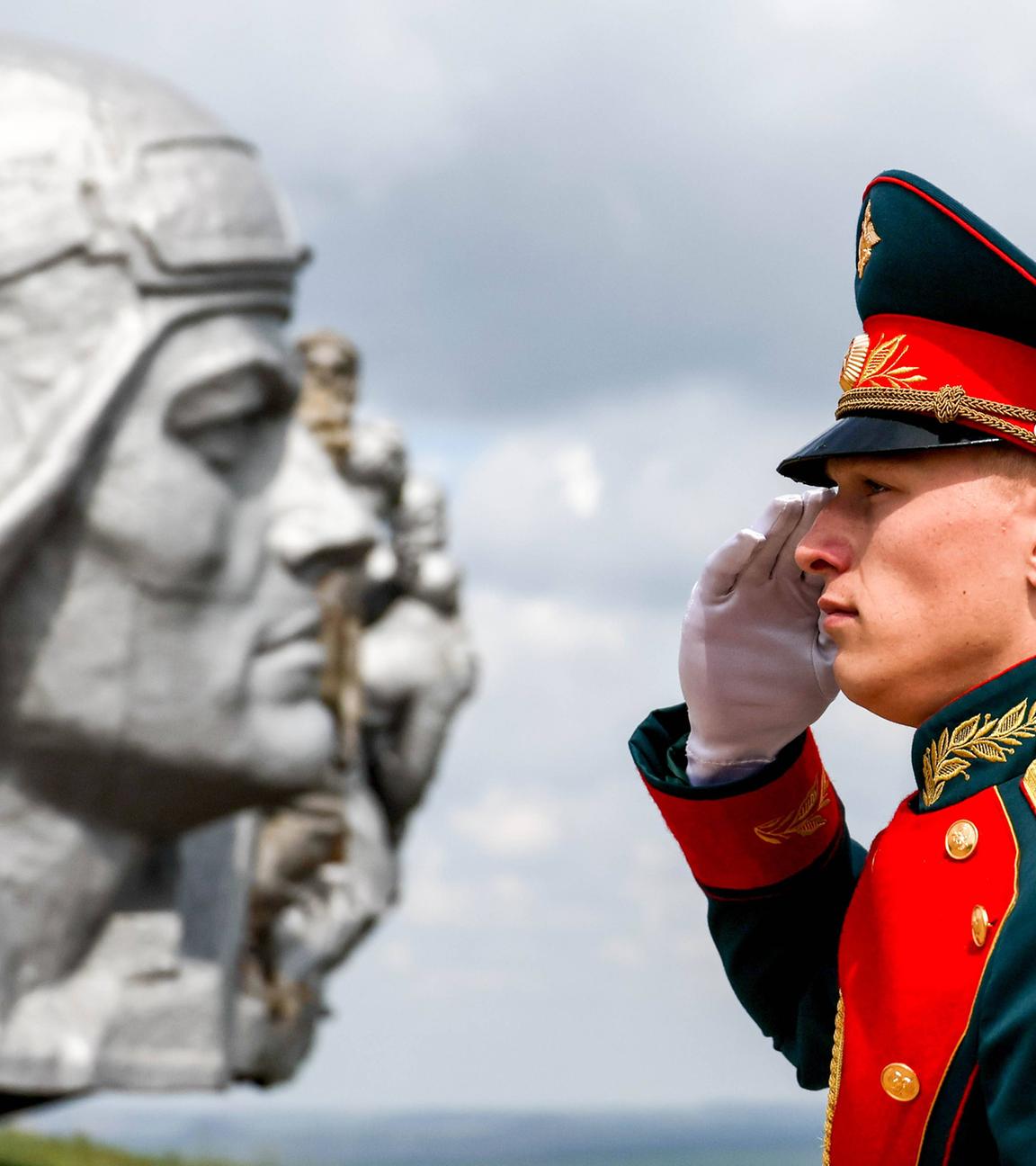 Ein russischer Soldat in Paradeuniform salutiert vor einem heroischen Soldatendenkmal.