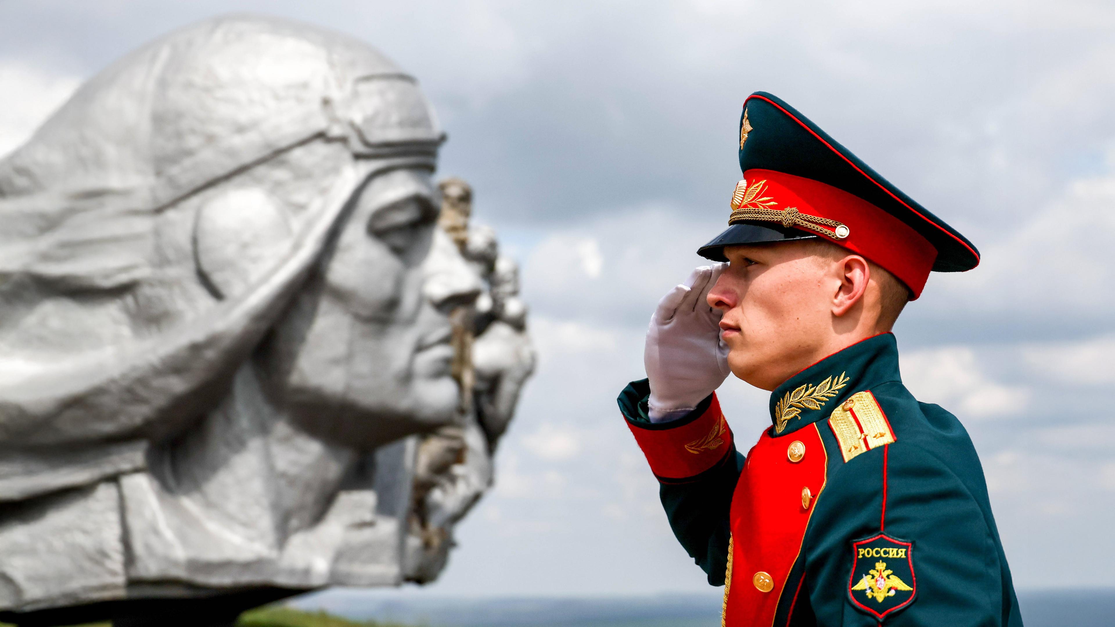 Ein russischer Soldat in Paradeuniform salutiert vor einem heroischen Soldatendenkmal.