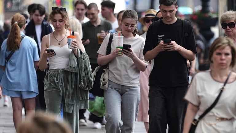 Fußgänger schauen auf ihre Handys, während sie durch St. Petersburg, Russland, gehen, Archivbild