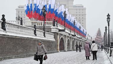 People walk past Russian flags fluttering in central Moscow on February 24, 2026.