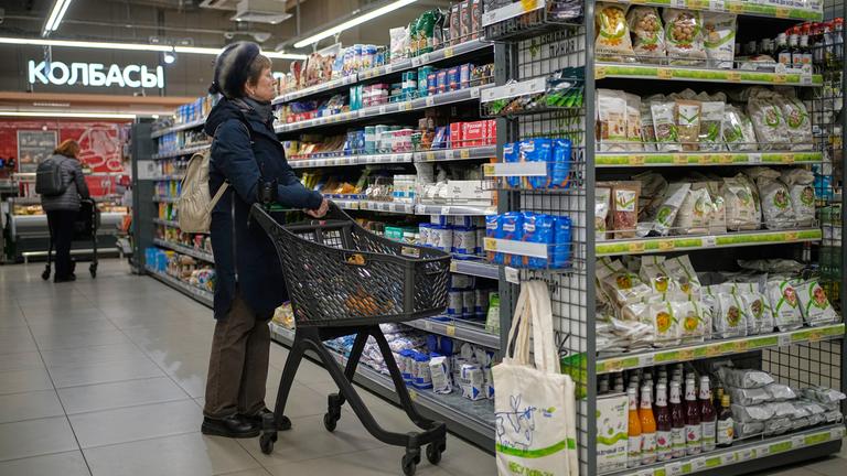Eine Frau wählt in einem russischen Supermarkt Produkte aus einem Regal aus.