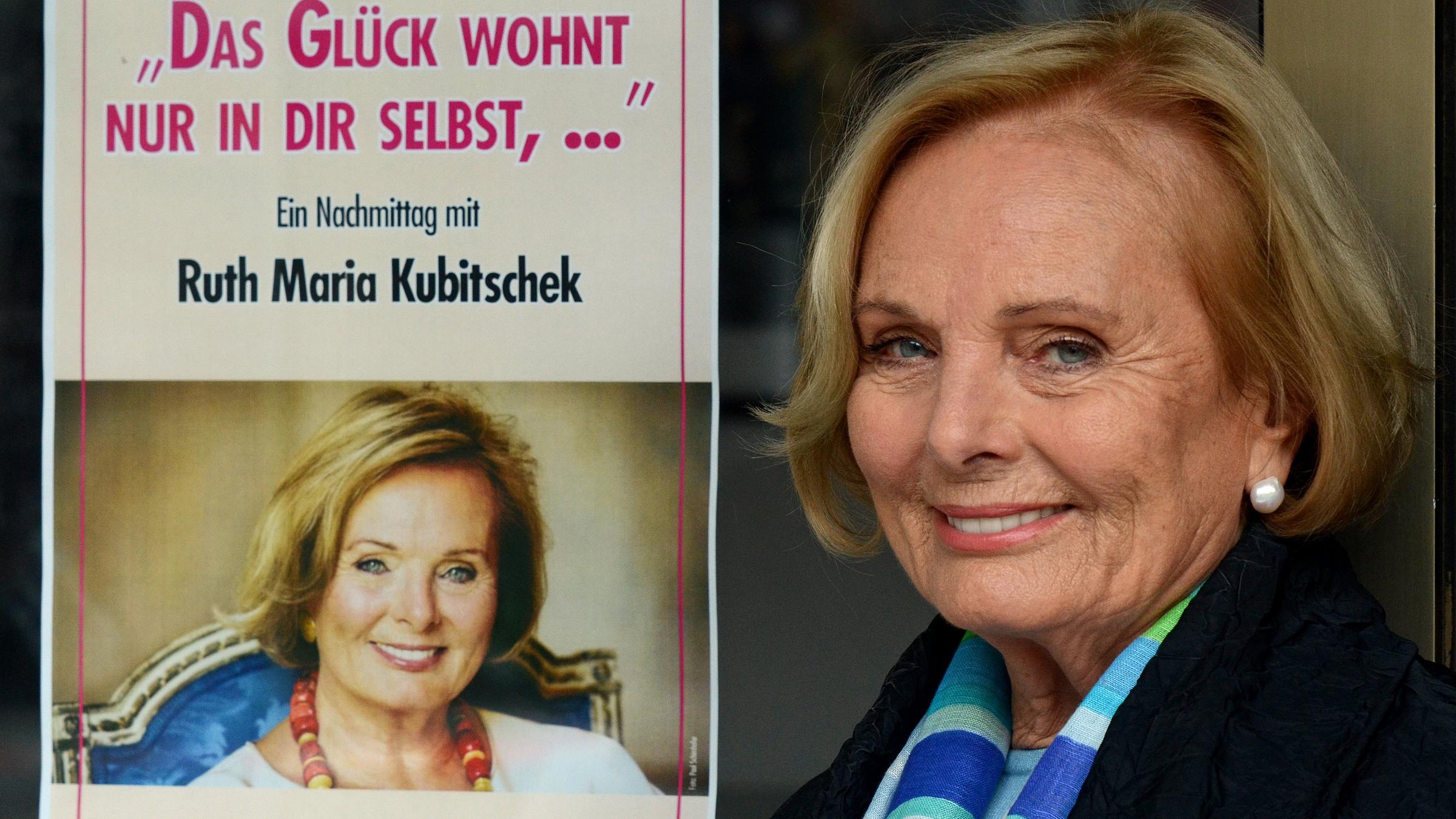 Die Schauspielerin Ruth Maria Kubitschek posiert neben einem Plakat zu ihrer Lesung "Das Glück wohnt nur in dir selbst,... Ein Nachmittag mit Ruth Maria Kubitschek". 