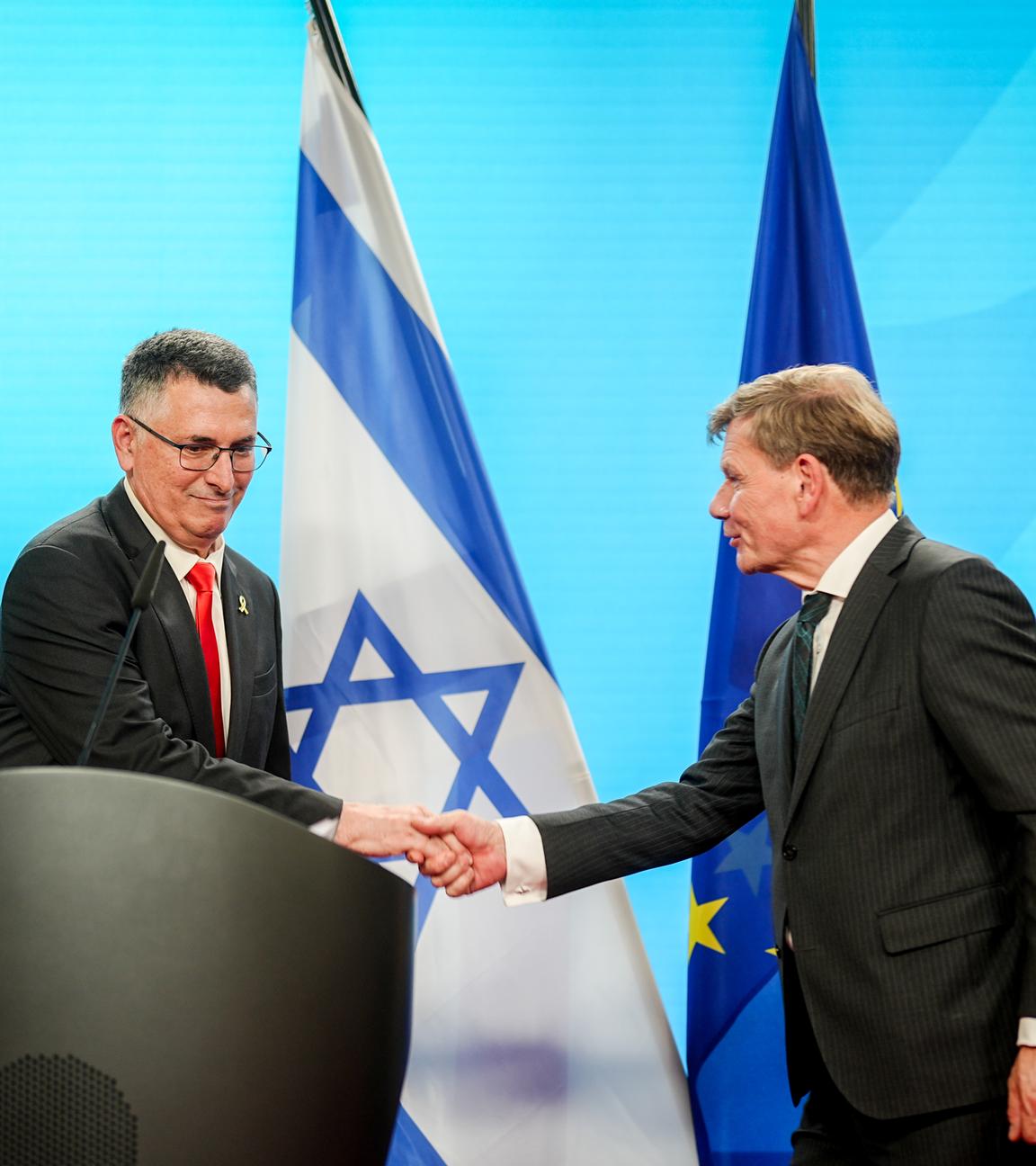 Gideon Saar und Johann Wadephul schütteln sich bei Pressekonferenz die Hände. Hinter ihnen die deutsche, israelische und EU-Flagge.
