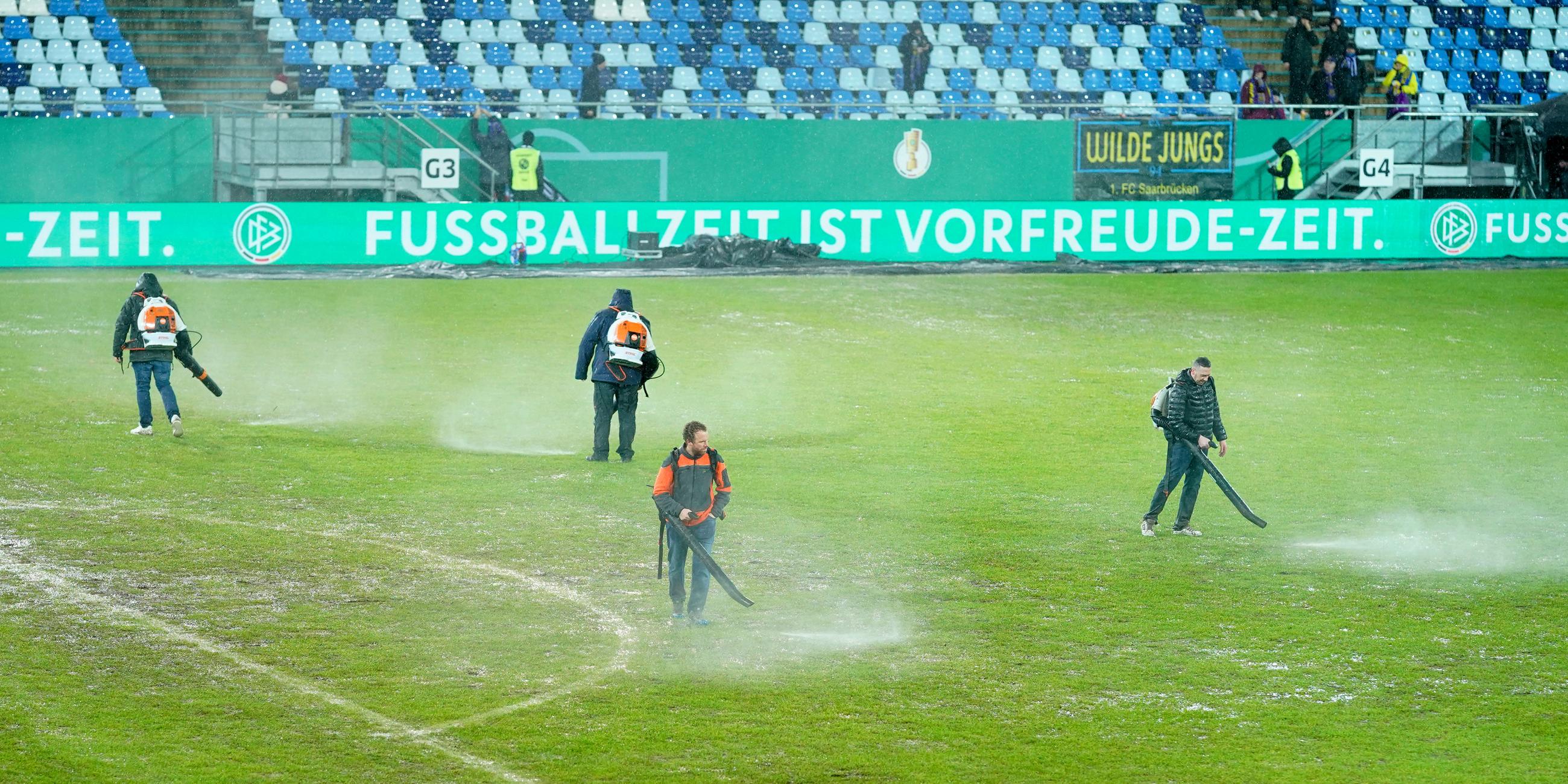 Saarland, Saarbrücken: Fußball: DFB-Pokal, 1. FC Saarbrücken - Bor. Mönchengladbach, Viertelfinale im Ludwigspark-Stadion. Arbeiter versuchen, Wasserlachen vom Spielfeld zu entfernen.