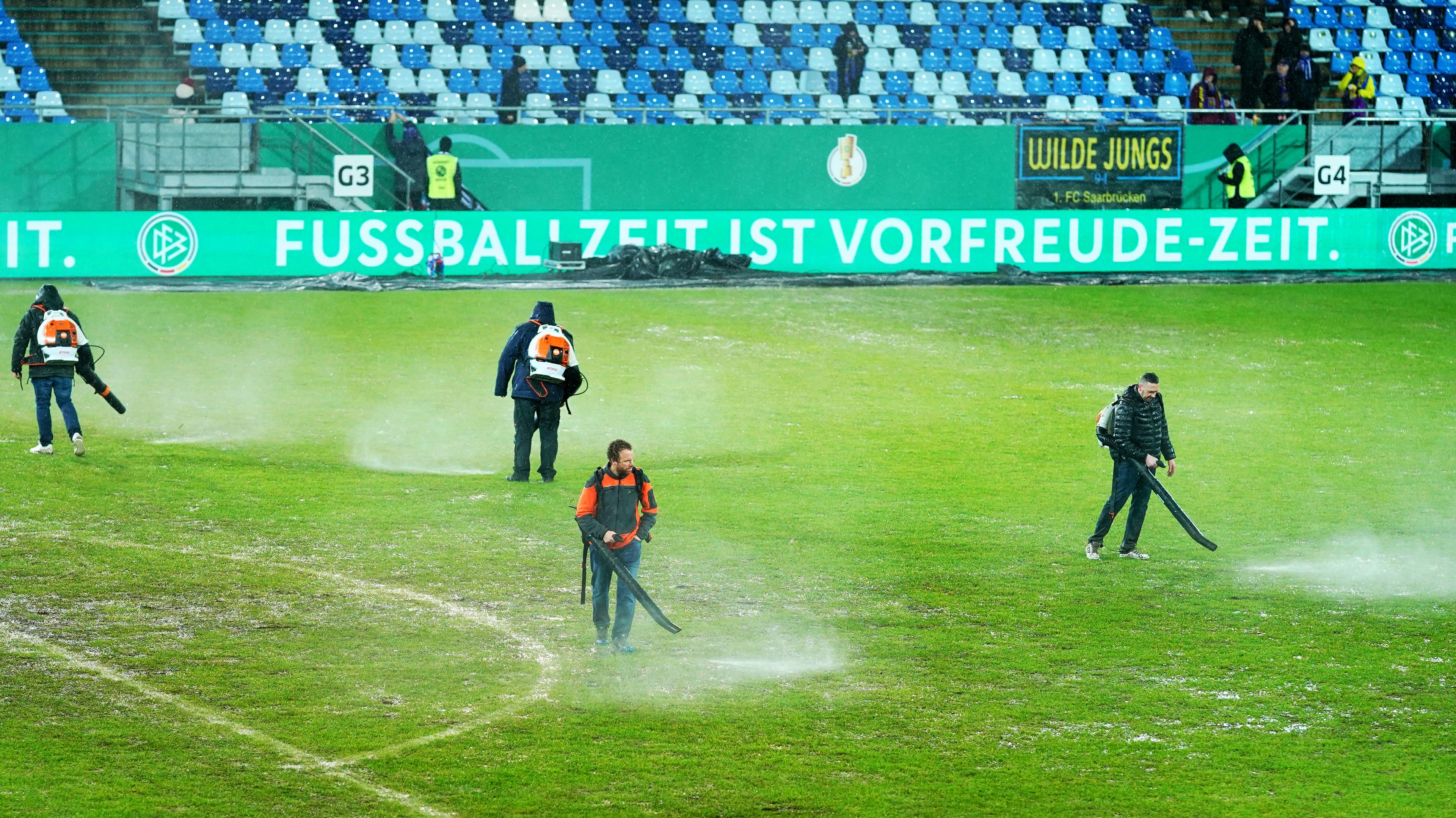 Arbeiter versuchen, Wasserlachen vom Spielfeld zu entfernen.