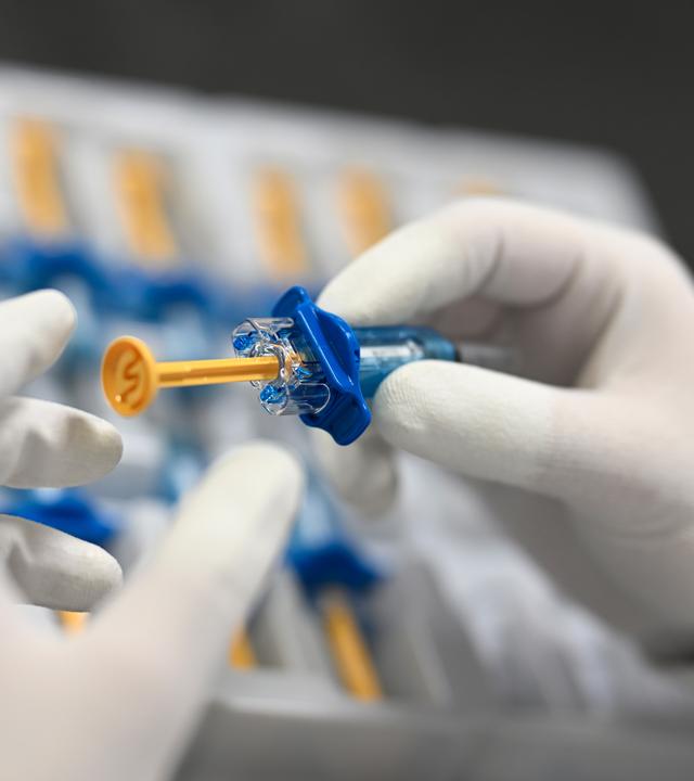 Ein Mitarbeiter von Vetter Pharma kontrolliert in der Produktion die korrekte Montage von Anbauteilen an einer Spritze.
