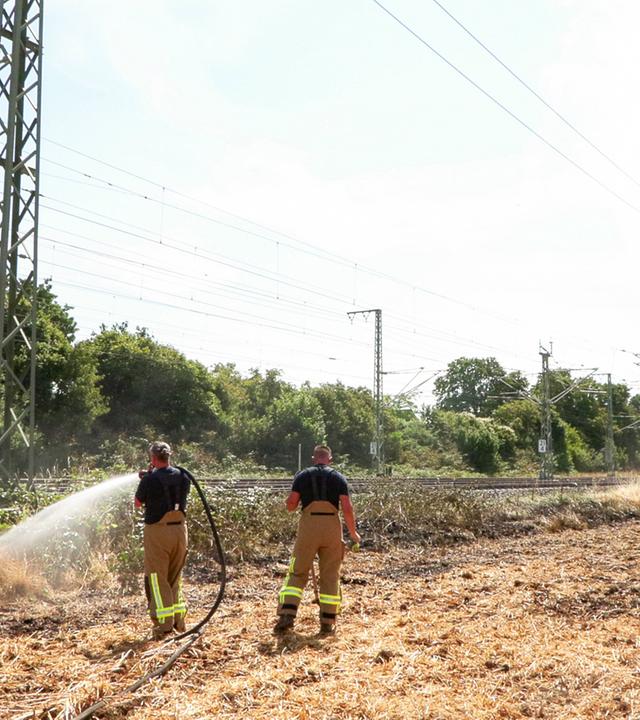 Einsatzkräfte der Feuerwehr löschen einen Böschungsbrand an einer Bahnstrecke.