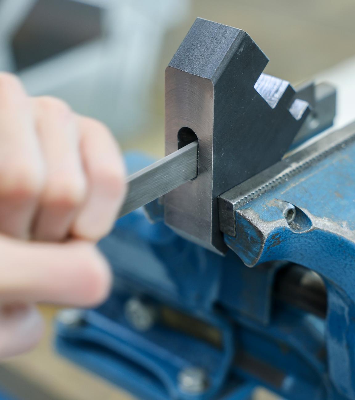 Die Hand eines Auszubildenden, der an einem Motorenträger aus Stahl feilt.