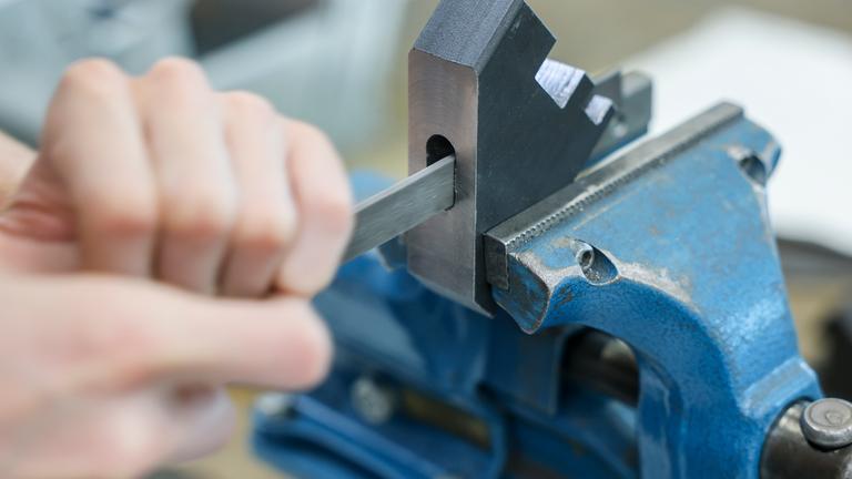 Die Hand eines Auszubildenden, der an einem Motorenträger aus Stahl feilt.