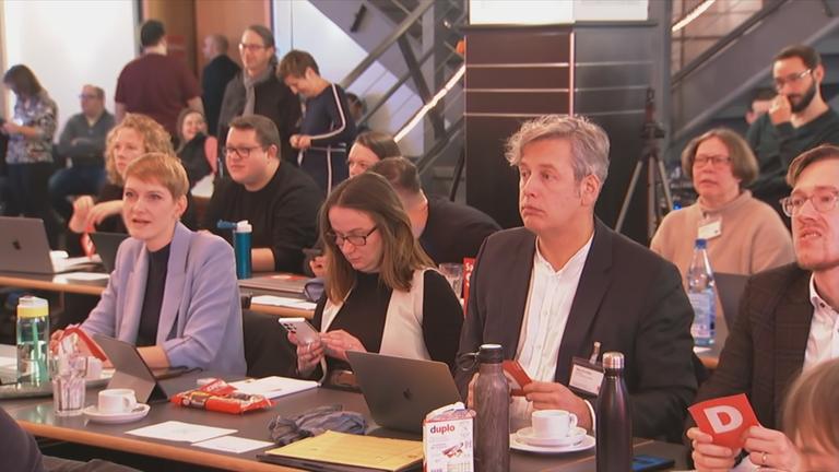 Auf dem Bild sieht man verschiedene Personen am Tisch sitzen.