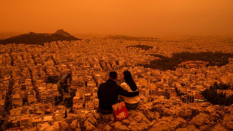 Ein Paar sitzt in Athen auf dem Tourkovounia-Hügel, während Südwinde Wellen von Saharastaub herantragen