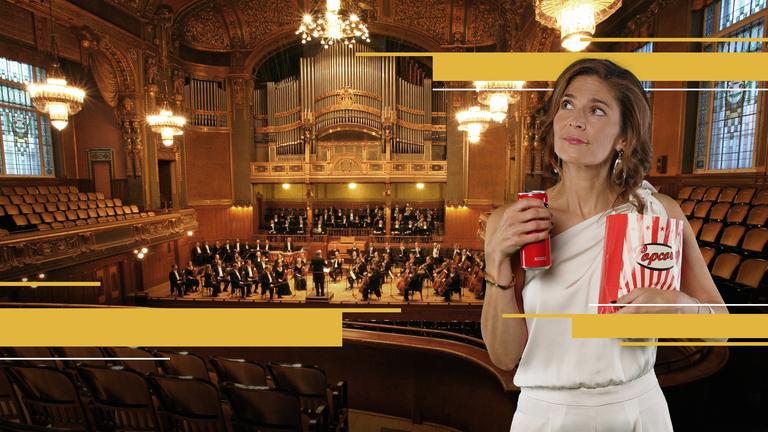 Katty Salié mit geniesserischen Blick mit Getränkedose und Popcorntüte in einem opulenten Konzertsaal.