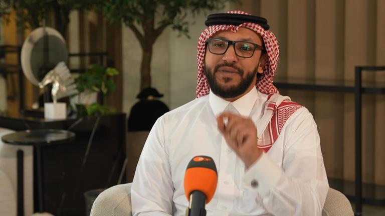 Salman Al-Ansari sitzt während eines Interviews auf einem Sessel und spricht in ein Mikrofon.