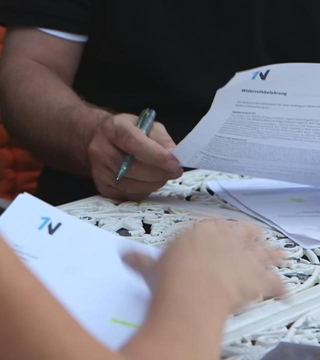 Zwei Menschen sitzen an einem Tisch und schauen sich Verträge an.