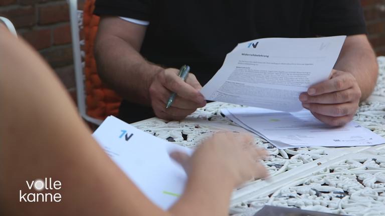 Zwei Menschen sitzen an einem Tisch und schauen sich Verträge an.