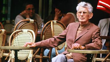 Ein älterer Mann mit Brille und grauen Haaren sitzt in einem Korbstuhl in einem Café.