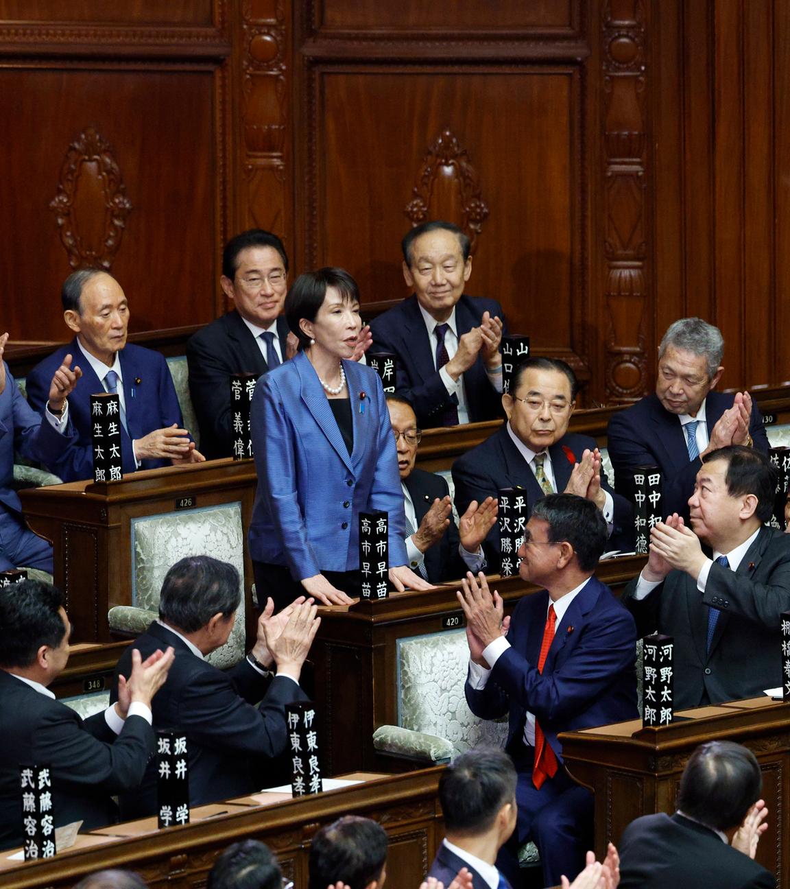 Es ist die neue Ministerpräsidentin zu sehen, wie sie im Kongress Japans steht. Um sie herum sind andere Abgeordnete.