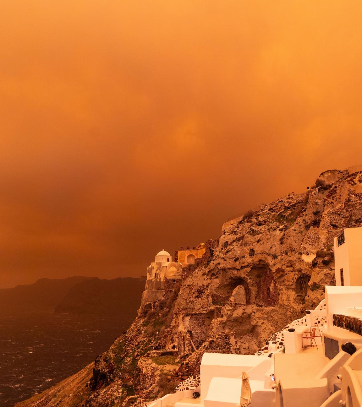 Kräftiger Sturm trägt Sand aus Afrika über die Insel Santorin und färbt den Himmel orangerot ein.